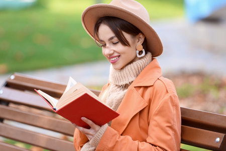 Beautiful woman reading book on wooden bench outdoorsの写真素材