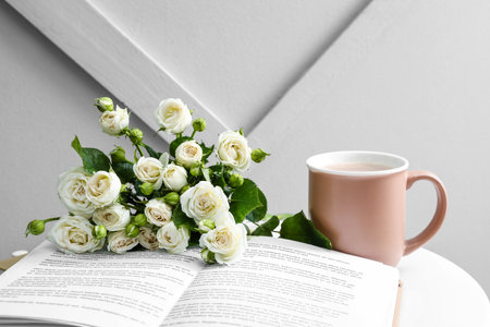 Bouquet of beautiful roses, book and cup with coffee on table near light wallの写真素材