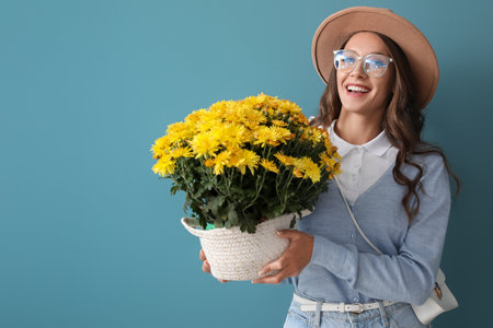 Young fashionable woman holding beautiful Chrysanthemum flowers on blue backgroundの写真素材