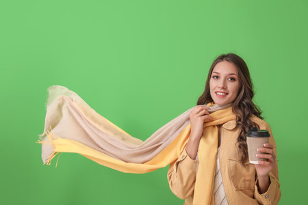 Beautiful smiling woman with stylish scarf holding paper cup on green backgroundの写真素材