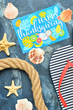 Rope, seashells, flip flops and paper card with text HAPPY THANKSGIVING on color background, closeup