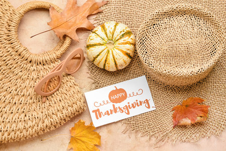 Wicker bag, hat, dry leaves, pumpkin, sunglasses and paper card with text HAPPY THANKSGIVING on color backgroundの写真素材