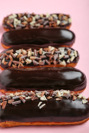 Delicious chocolate eclairs on pink background, closeup