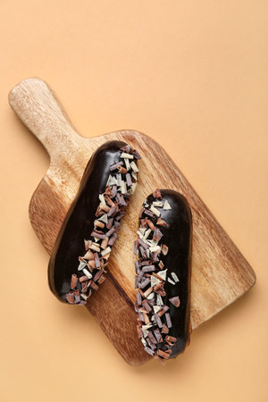 Wooden board with tasty eclairs on color background
