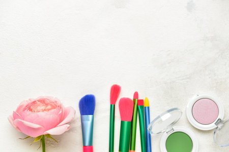 Makeup brushes, eye shadows and rose flower on light backgroundの写真素材