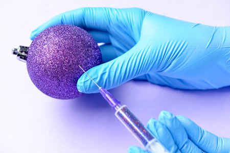 Woman in medical gloves injecting vaccine into Christmas ball on color background, closeupの写真素材
