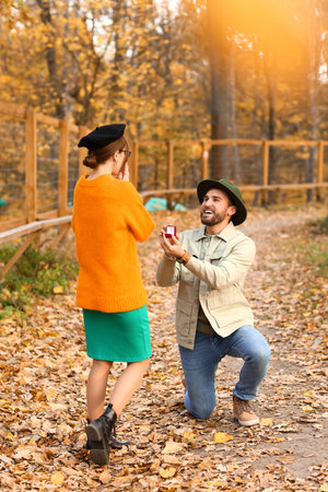 Young man proposing to his beloved in beautiful autumn parkの写真素材