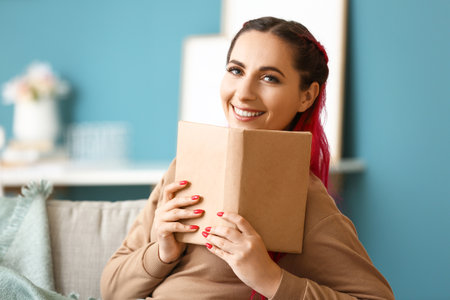 Beautiful woman with book sitting on sofa at homeの写真素材