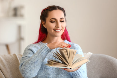 Beautiful woman in blue sweater with book on sofa at homeの写真素材