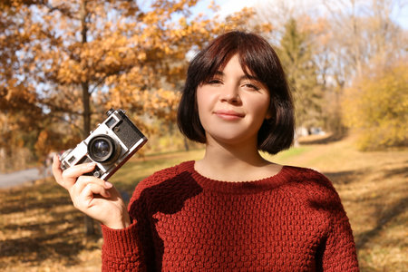 Young woman with photo camera enjoying sunny day in autumn park