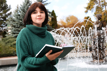 Young beautiful woman with book near fountain in autumn parkの写真素材