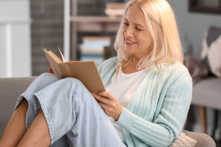 Beautiful mature woman reading book at home on autumn dayの写真素材