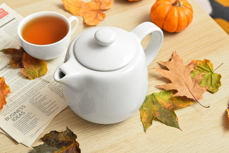 Tea pot, cup of hot beverage, newspaper and autumn leaves on wooden backgroundの写真素材