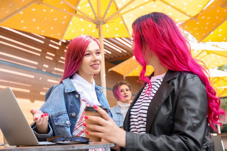 Beautiful women with cup of coffee and laptop at table in street cafeの写真素材