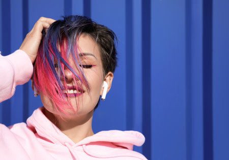 Beautiful woman with dyed hair and earphones on blue background, closeupの写真素材