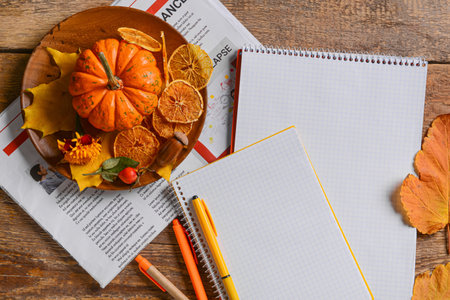 Plate with pumpkin, food, fallen leaves, newspaper and stationery on wooden background