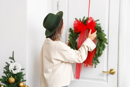 Young fashionable woman decorating white door for Christmas in roomの写真素材