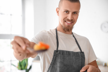 Handsome young man holding spatula with fried vegetables in kitchen, closeupの写真素材