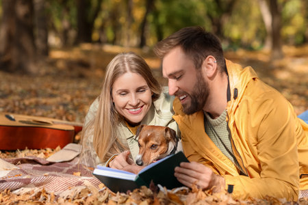 Lovely couple with Jack Russel terrier reading book in park on autumn dayの写真素材