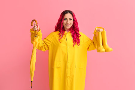 Beautiful woman in raincoat, with gumboots and umbrella on color backgroundの写真素材