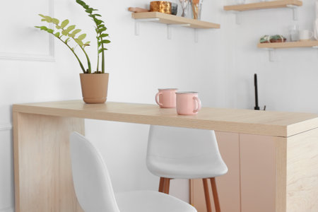 Pink cups and houseplant on dining table in light kitchenの写真素材