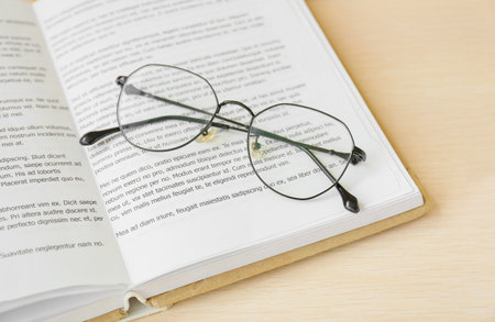 Book with eyeglasses on wooden tray, closeup