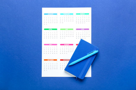 Paper calendar for 2022 year, notebook and pen on color background