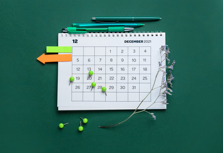 Flip paper calendar for December 2021, sticky notes, pens, pins and flower branch on green backgroundの写真素材