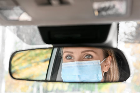 Reflection of female driver wearing medical mask in car rear view mirrorの写真素材
