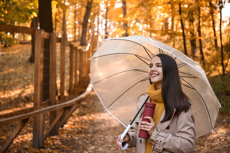 Young smiling woman with umbrella and bottle in autumn park on sunny dayの写真素材