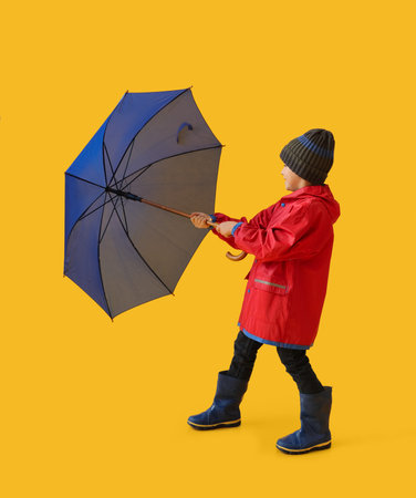 Little boy in raincoat and umbrella on color background