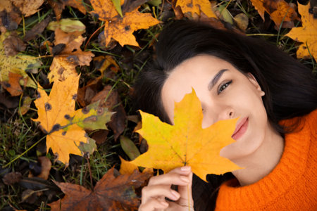 beautiful woman lying on ground and holding autumn leafの写真素材