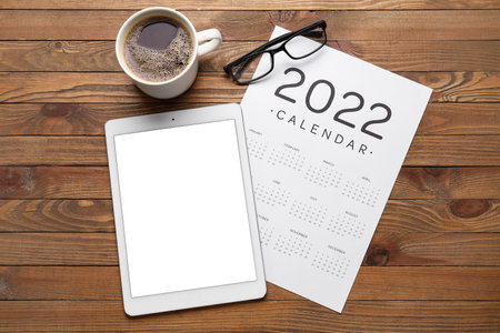 Paper calendar for 2022 year, eyeglasses, cup of coffee and tablet computer on wooden backgroundの写真素材