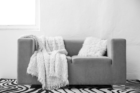 Gray sofa with white blanket and cushion near light wallの写真素材