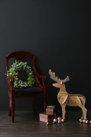 Wooden reindeer, armchair, Christmas wreath and gift boxes near dark wallの写真素材
