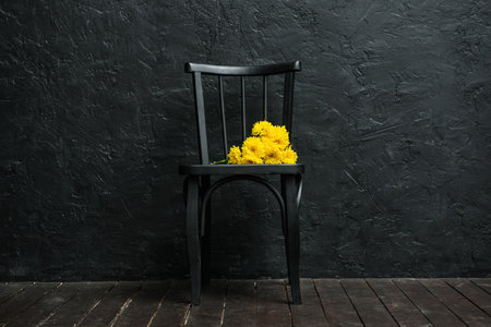 Black chair with yellow flowers near dark wallの写真素材