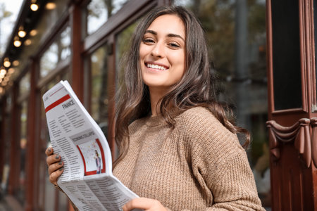 Beautiful young woman with newspaper on city street