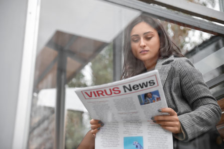 Beautiful young woman reading newspaper on bus stopの写真素材
