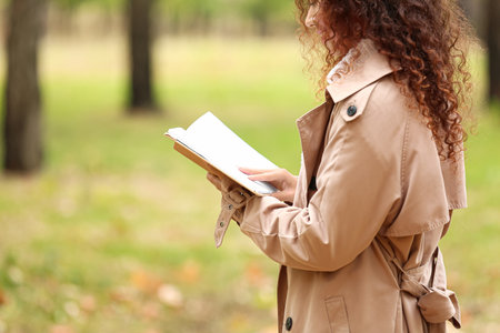 Young African-American woman reading book in autumn parkの写真素材