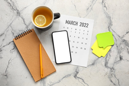 Flat lay with notebook, smartphone, cup of tea and calendar on marble backgroundの写真素材