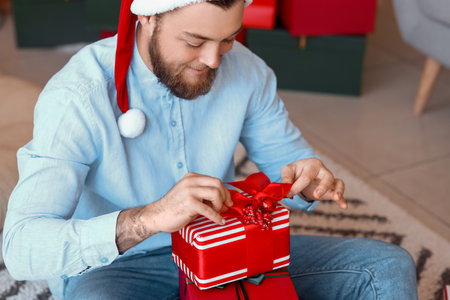 Handsome man opening Christmas gifts at homeの写真素材