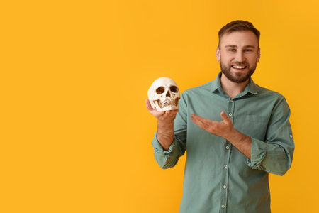 Handsome man with human skull on yellow backgroundの写真素材