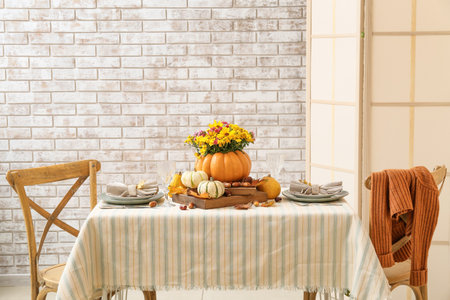 Beautiful bouquet of autumn flowers in pumpkin on served table near brick wallの写真素材