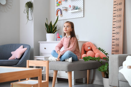 Cute little girl sitting on ottoman at homeの写真素材