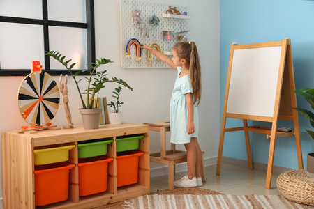 Cute little girl taking toy rainbow from hanging peg board on light wallの写真素材