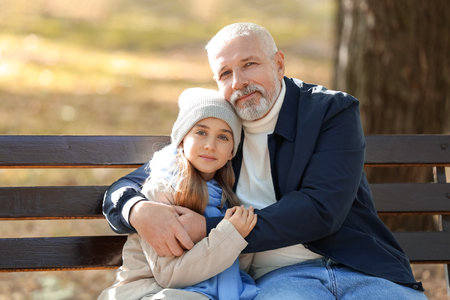 Little girl with her grandfather hugging on bench in parkの写真素材
