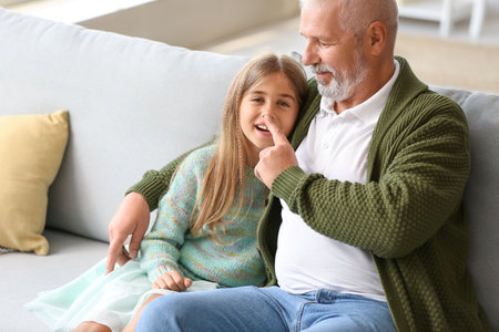 Senior man touching his little granddaughter's nose at homeの写真素材