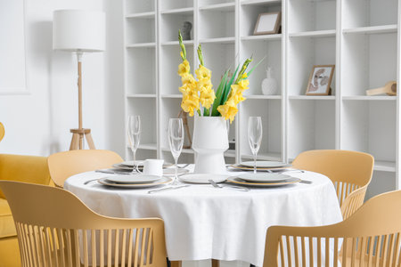 Beautiful table setting and vase with Gladiolus flowers in dining roomの写真素材