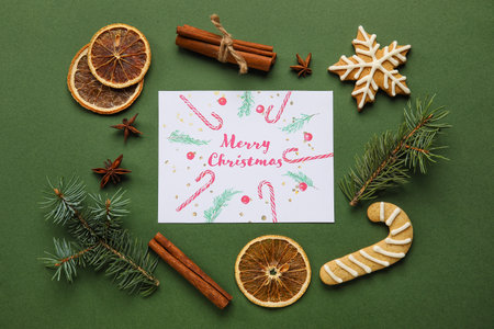 Frame made of fir tree branches, cookies and greeting card with text MERRY CHRISTMAS on green backgroundの写真素材
