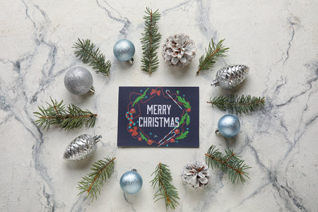 Frame made of fir tree branches, decor and greeting card with text MERRY CHRISTMAS on light backgroundの写真素材